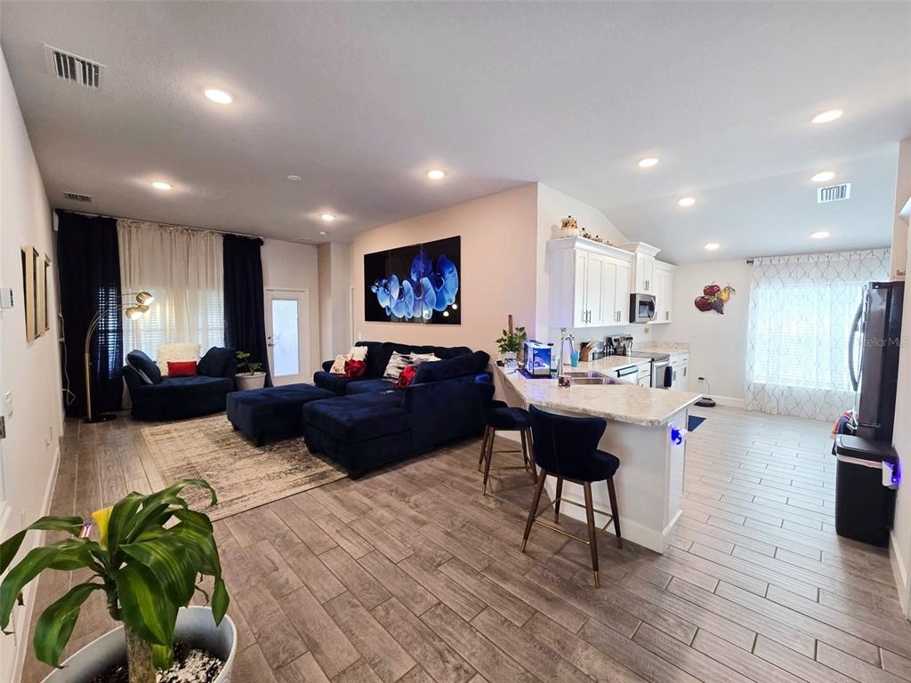 An open-concept living room and kitchen featuring dark blue furniture, tile flooring, and white cabinetry — 38136 COUNTRYSIDE PLACE, DADE CITY, FL