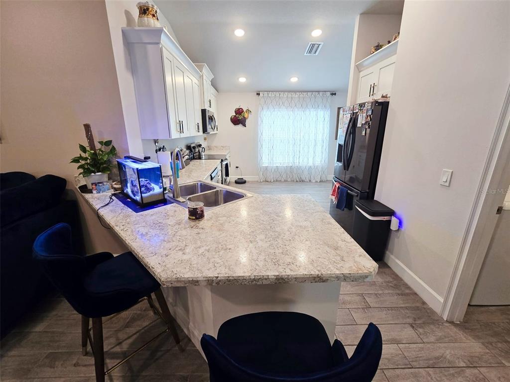 A kitchen features a granite-topped peninsula, white cabinetry, stainless steel appliances, and tile flooring — 38136 COUNTRYSIDE PLACE, DADE CITY, FL