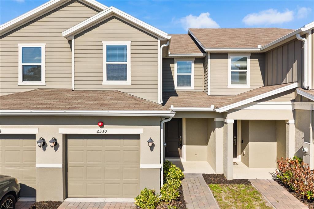 The exterior of a two-story townhouse features tan siding, a garage, and a paved walkway — 2330 CARRABELLE WAY, SANFORD, FL