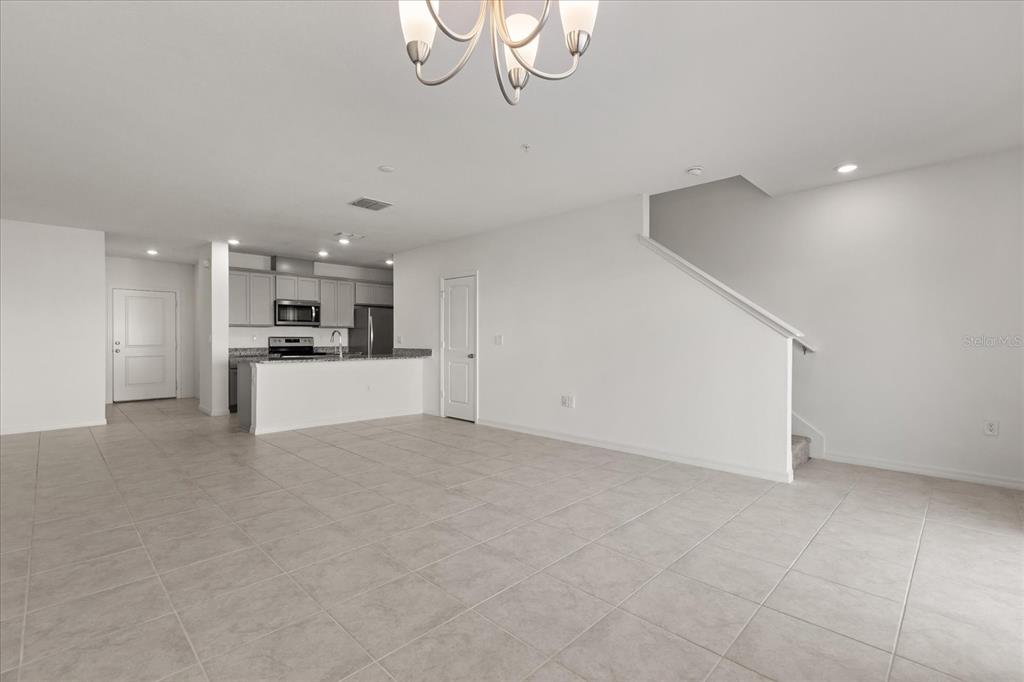 An open-concept living area features light tile flooring, a kitchen with gray cabinets, and stairs — 2330 CARRABELLE WAY, SANFORD, FL
