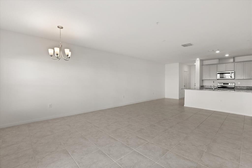An open-concept dining area with tile flooring and a chandelier leads to a kitchen — 2330 CARRABELLE WAY, SANFORD, FL