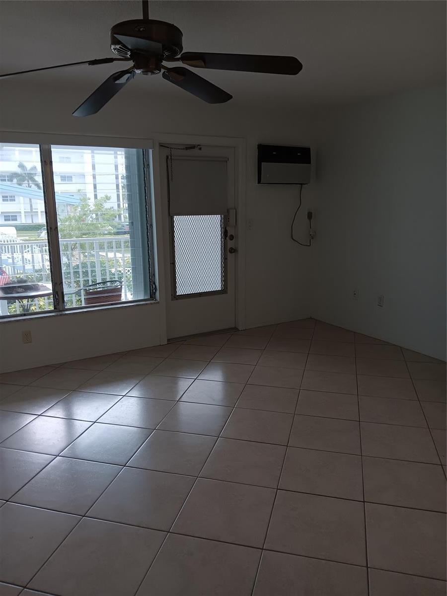 An empty room features beige tile flooring, a ceiling fan, and a door to a balcony — 1110 N Riverside Drive # 26, Pompano Beach FL 33062, POMPANO BEACH, FL