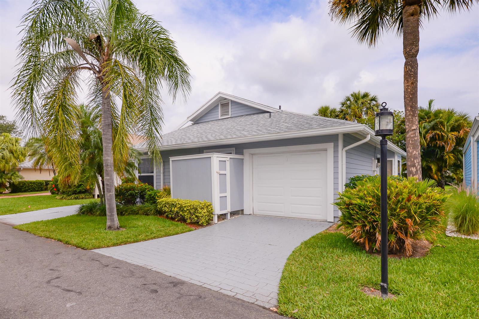 A light blue house with a white garage door, a paved driveway, and palm trees — 3267 NE Catamaran Terrace, Jensen Beach FL 34957, JENSEN BEACH, FL