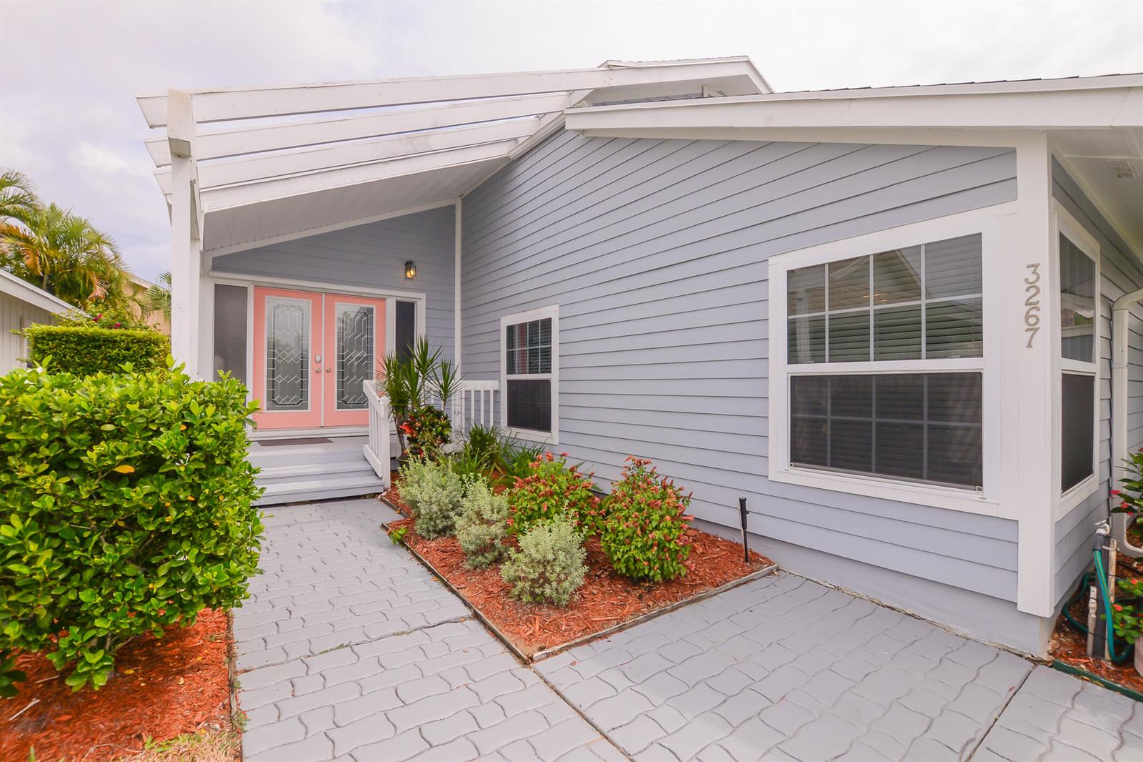 A light blue house exterior features a pink double front door and a paved walkway — 3267 NE Catamaran Terrace, Jensen Beach FL 34957, JENSEN BEACH, FL