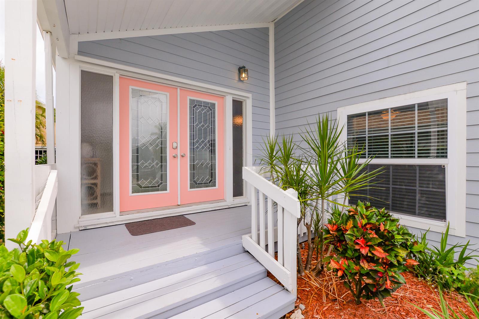 A light blue house exterior features a pink double front door and a wooden porch — 3267 NE Catamaran Terrace, Jensen Beach FL 34957, JENSEN BEACH, FL