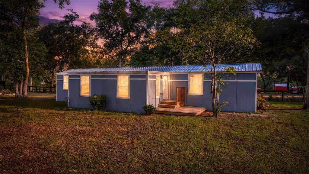 A blue single-wide mobile home with a metal roof sits on a grassy lot at dusk — 23939 NE 121 LANE, SALT SPRINGS, FL