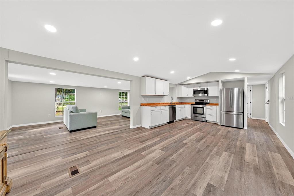 An open-concept kitchen and living area featuring white cabinets, wood countertops, and wood-look flooring — 23939 NE 121 LANE, SALT SPRINGS, FL