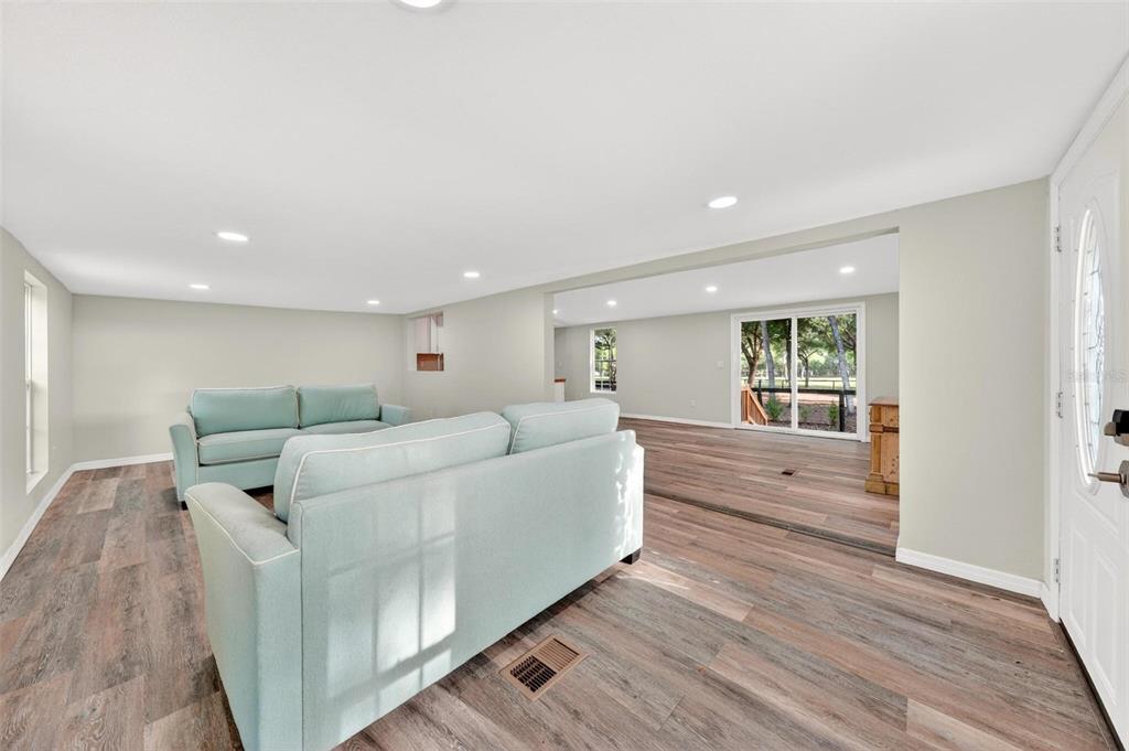A living room with light blue sofas, wood-look flooring, and a sliding glass door — 23939 NE 121 LANE, SALT SPRINGS, FL