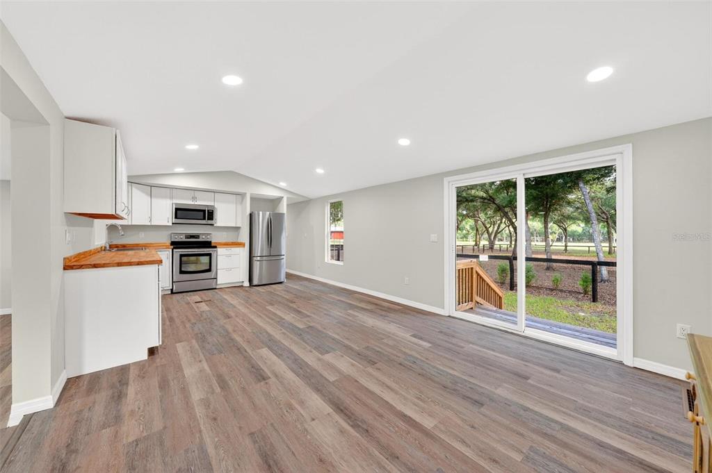 A kitchen with white cabinets and wood countertops opens to a living area with sliding doors — 23939 NE 121 LANE, SALT SPRINGS, FL