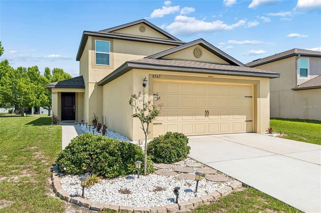 A two-story house with a beige stucco exterior, a two-car garage, and a front garden — 8567 INDIAN LAUREL LANE, BROOKSVILLE, FL