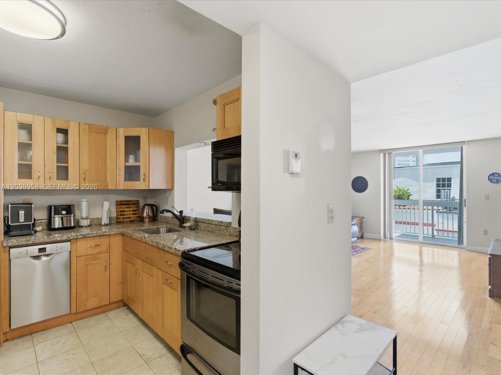 A kitchen with light wood cabinets and granite countertops opens to a living area — 3588 Collins Ave # 504, Miami Beach FL 33140, MIAMI BEACH, FL