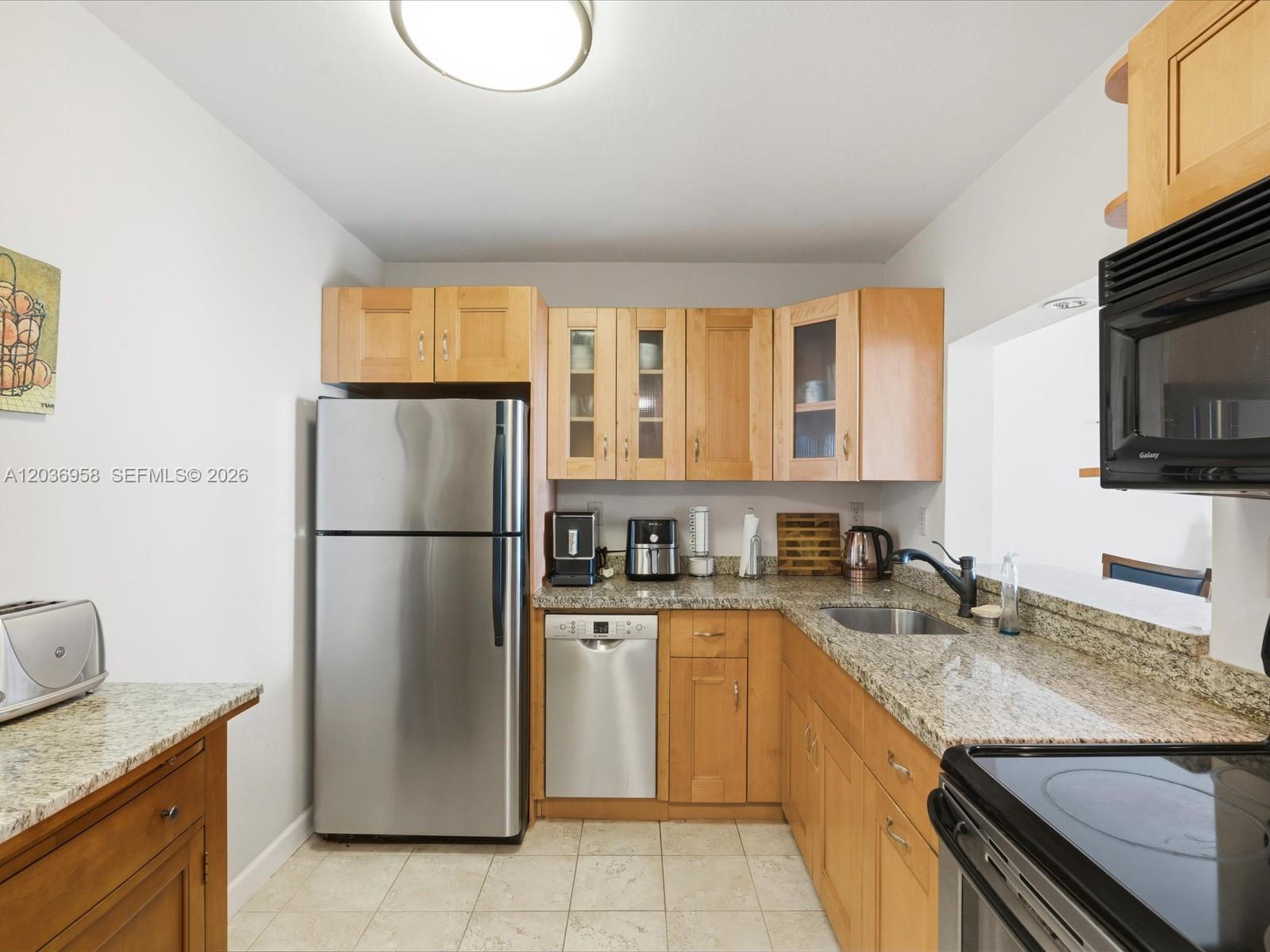 A kitchen features light wood cabinets, granite countertops, stainless steel appliances, and tile flooring — 3588 Collins Ave # 504, Miami Beach FL 33140, MIAMI BEACH, FL