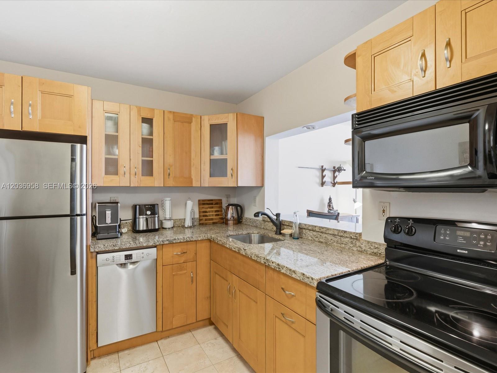A kitchen features light wood cabinets, granite countertops, stainless steel appliances, and a pass-through window — 3588 Collins Ave # 504, Miami Beach FL 33140, MIAMI BEACH, FL