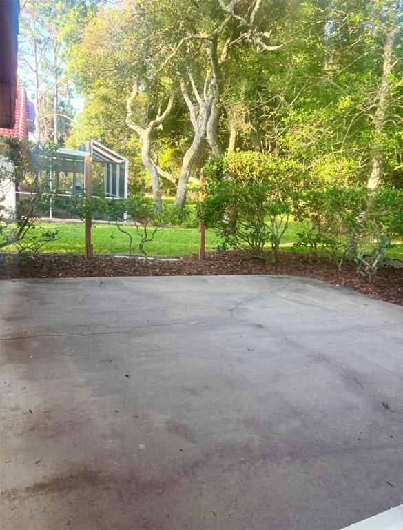 A concrete patio overlooks a grassy backyard with trees and a screened-in structure — 3 SAN JOSE DRIVE, PALM COAST, FL