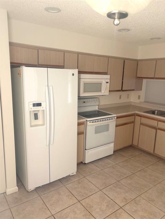A kitchen with light wood cabinets, white appliances, and tiled flooring — 3 SAN JOSE DRIVE, PALM COAST, FL