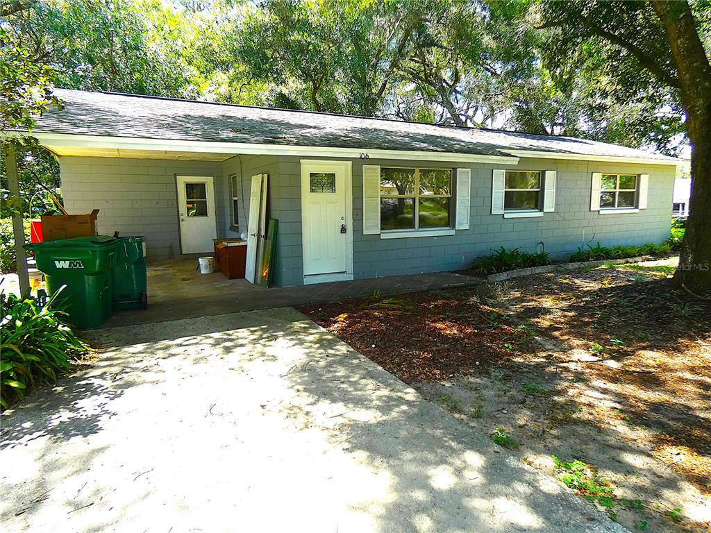 A gray, single-story house with a concrete driveway, two doors, and a large green trash bin — 106 WILLARD AVENUE, FRUITLAND PARK, FL