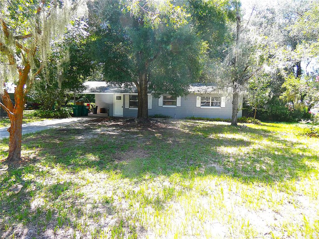 A single-story gray house with a carport sits behind a large tree in a yard — 106 WILLARD AVENUE, FRUITLAND PARK, FL