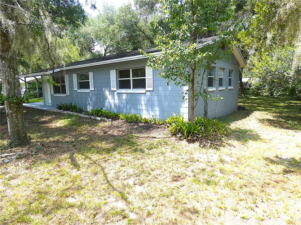 A gray, single-story house with a block exterior sits on a wooded lot — 106 WILLARD AVENUE, FRUITLAND PARK, FL