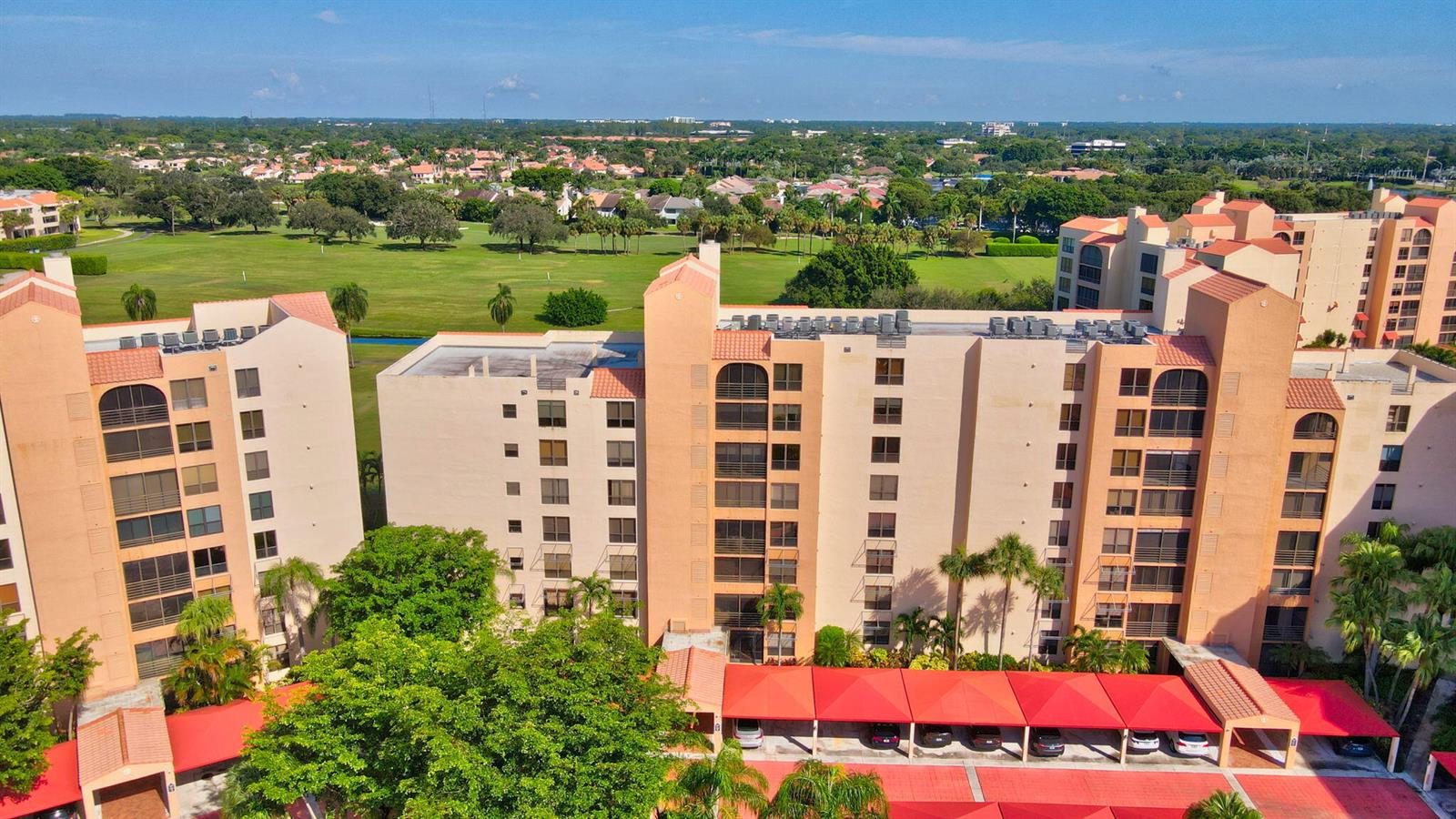 An aerial view shows a multi-story apartment complex with red-roofed carports and a golf course — 7225 Promenade Drive # 102, Boca Raton FL 33433, BOCA RATON, FL