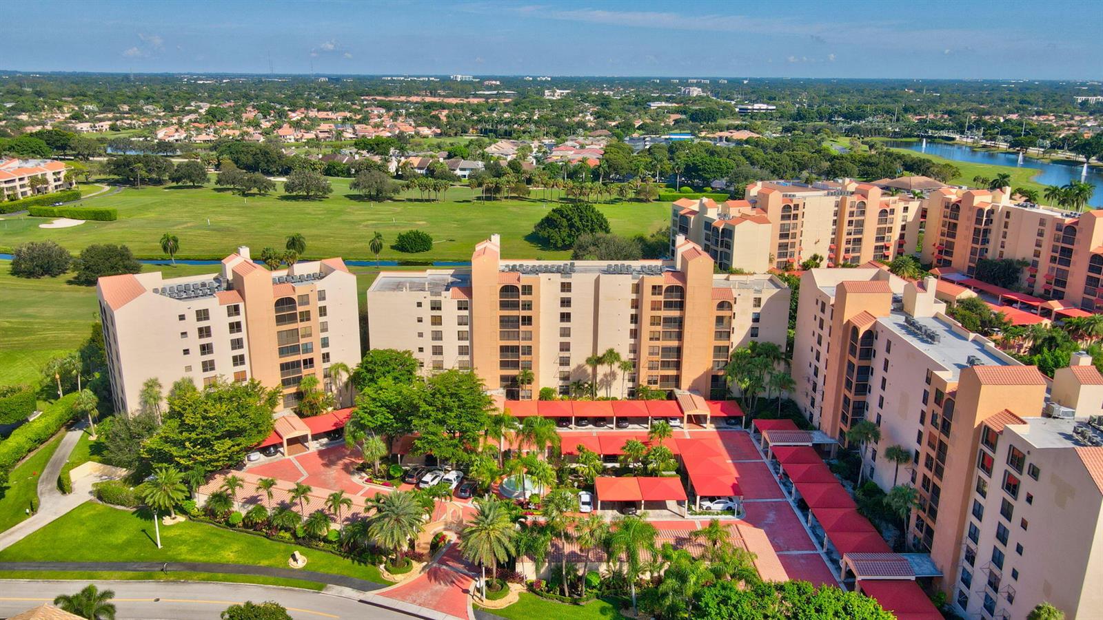 An aerial view shows a multi-story apartment complex with covered parking and a golf course — 7225 Promenade Drive # 102, Boca Raton FL 33433, BOCA RATON, FL
