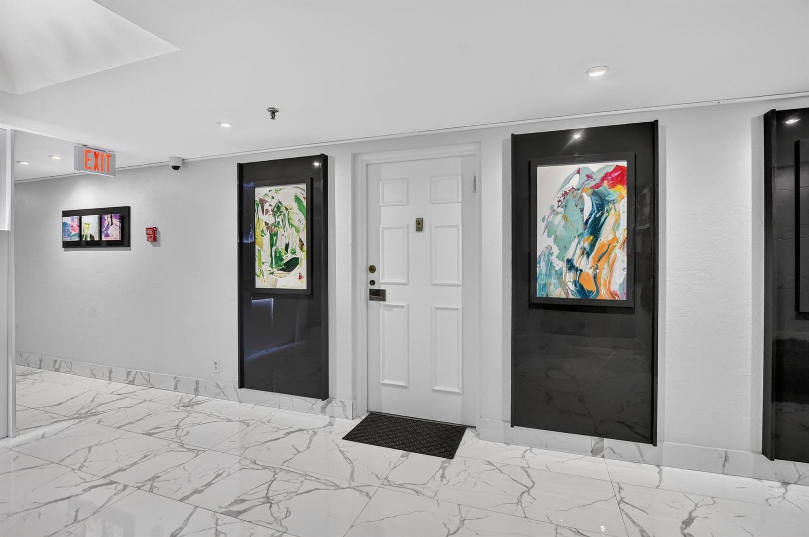 A white door is flanked by two framed abstract paintings on black panels in a hallway — 7225 Promenade Drive # 102, Boca Raton FL 33433, BOCA RATON, FL