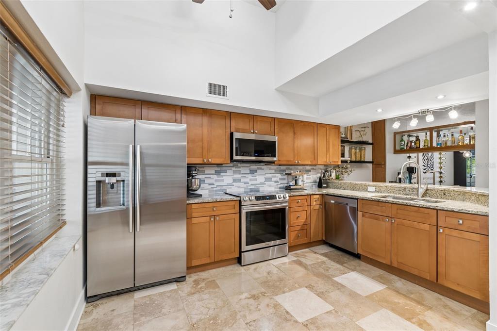 A kitchen with wood cabinets, stainless steel appliances, a tiled backsplash, and light-colored stone flooring — 2599 DOLLY BAY DRIVE UNIT 302, PALM HARBOR, FL