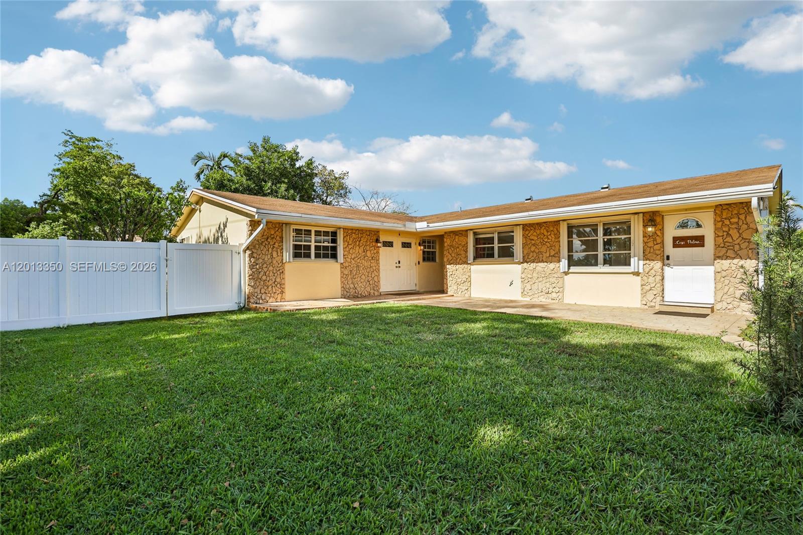 A single-story house with stone veneer siding and a white fence faces a grassy lawn — 108 SE 4th Ter, Dania Beach FL 33004, DANIA BEACH, FL