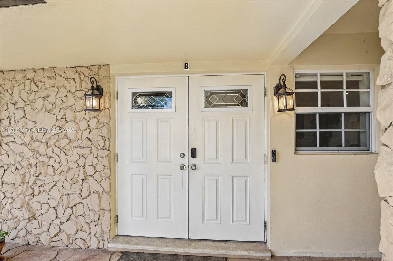 A double front door with glass inserts is flanked by stone siding and wall lanterns — 108 SE 4th Ter, Dania Beach FL 33004, DANIA BEACH, FL