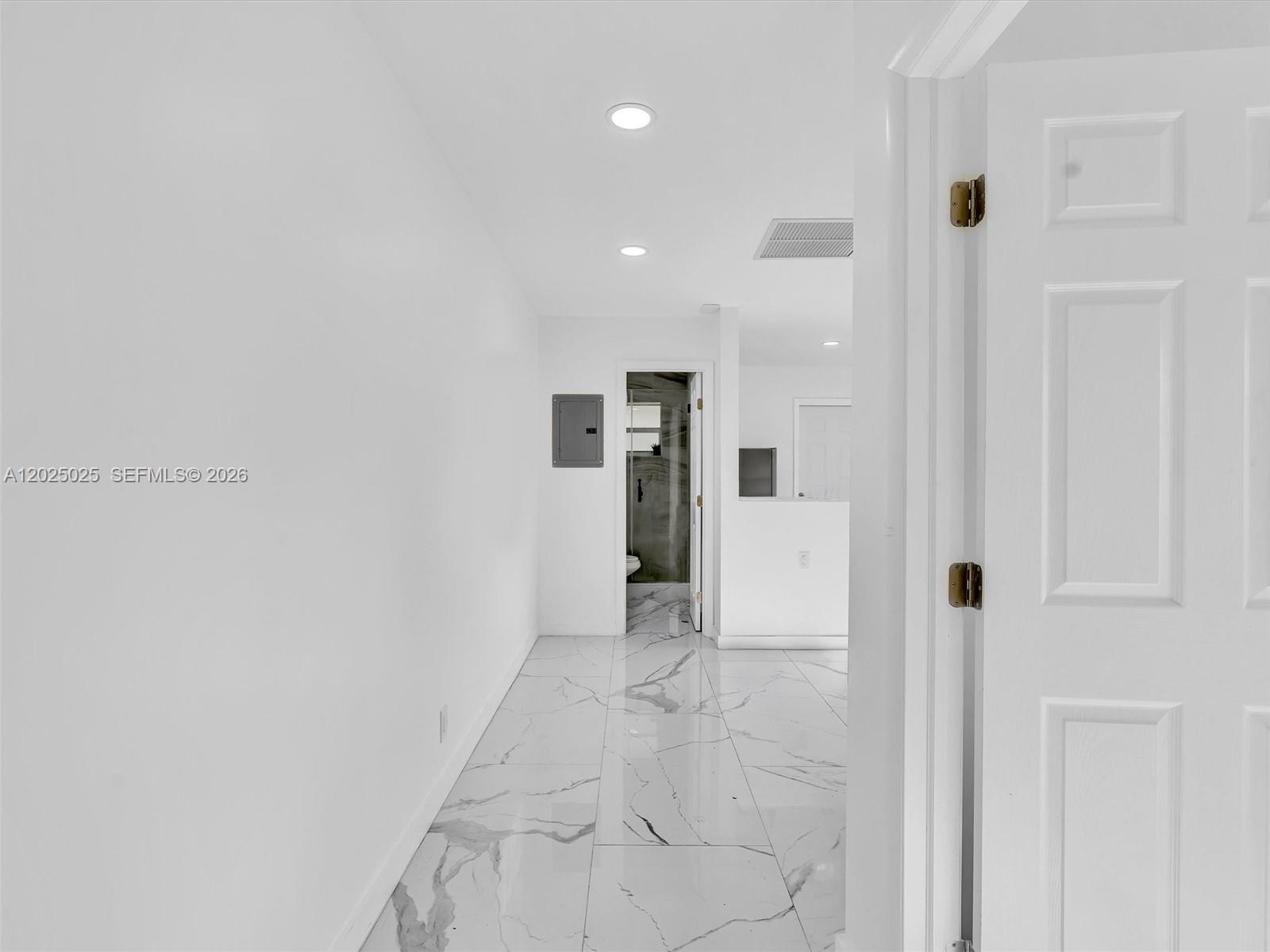 A hallway with white walls and white marble-patterned tile flooring leads to a bathroom — HOLLYWOOD, FL