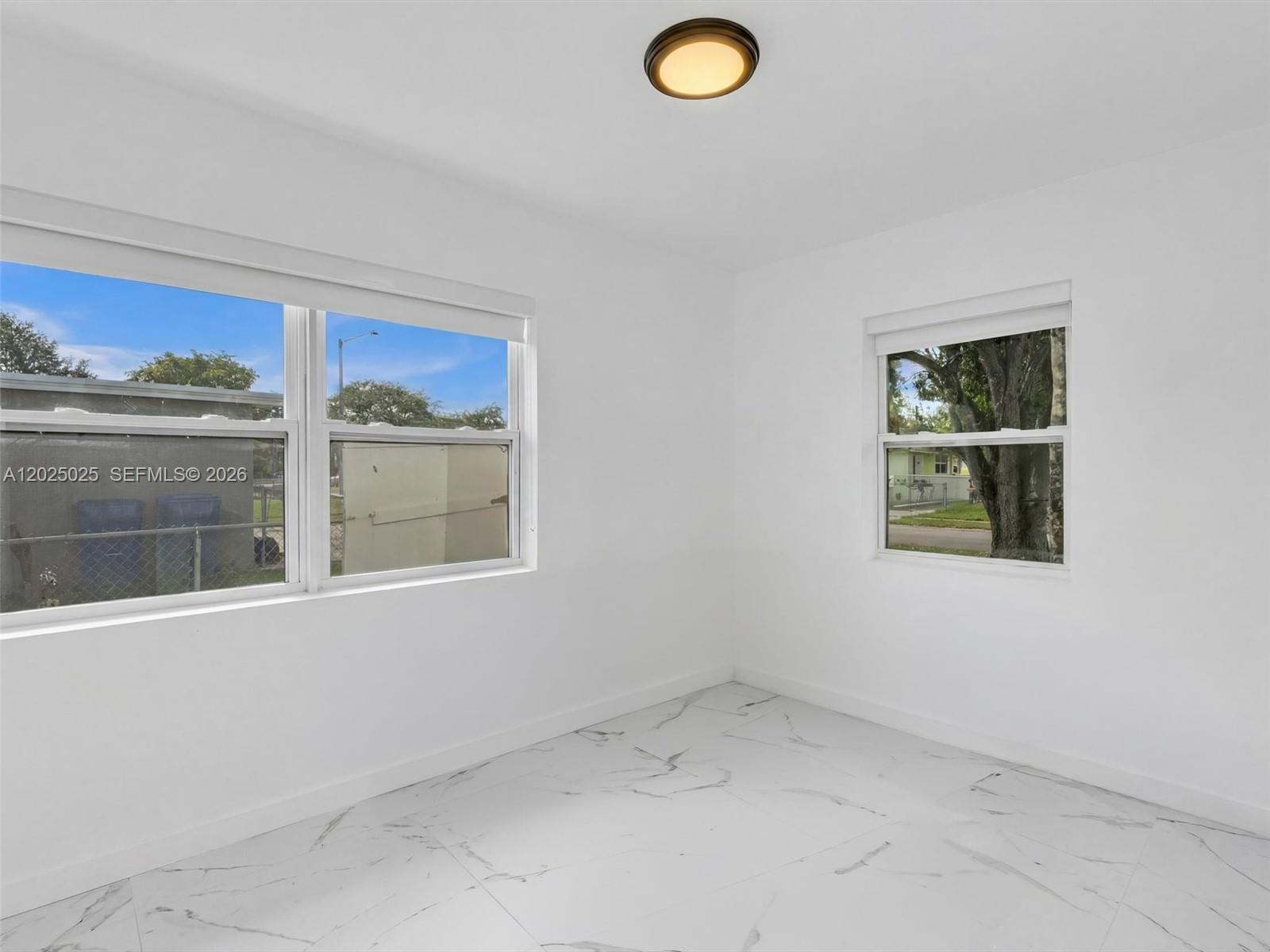 An empty room features white walls, white marble-patterned tile flooring, and two windows — HOLLYWOOD, FL