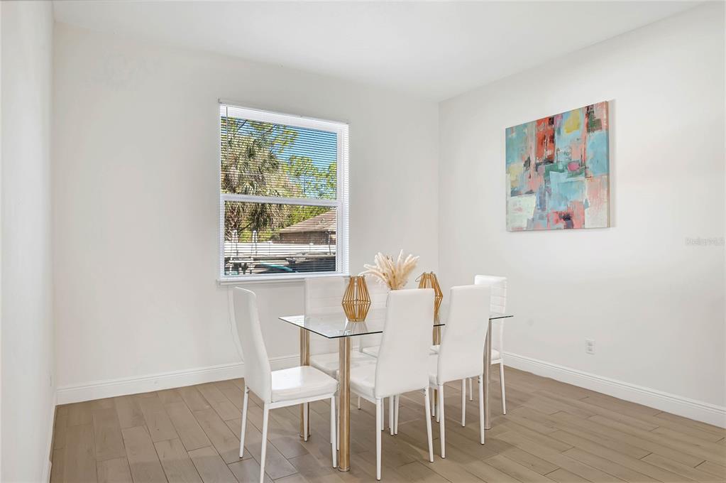 A dining room features a glass-top table, white chairs, light wood floors, and wall art — 643 FLYNN STREET SE, PALM BAY, FL
