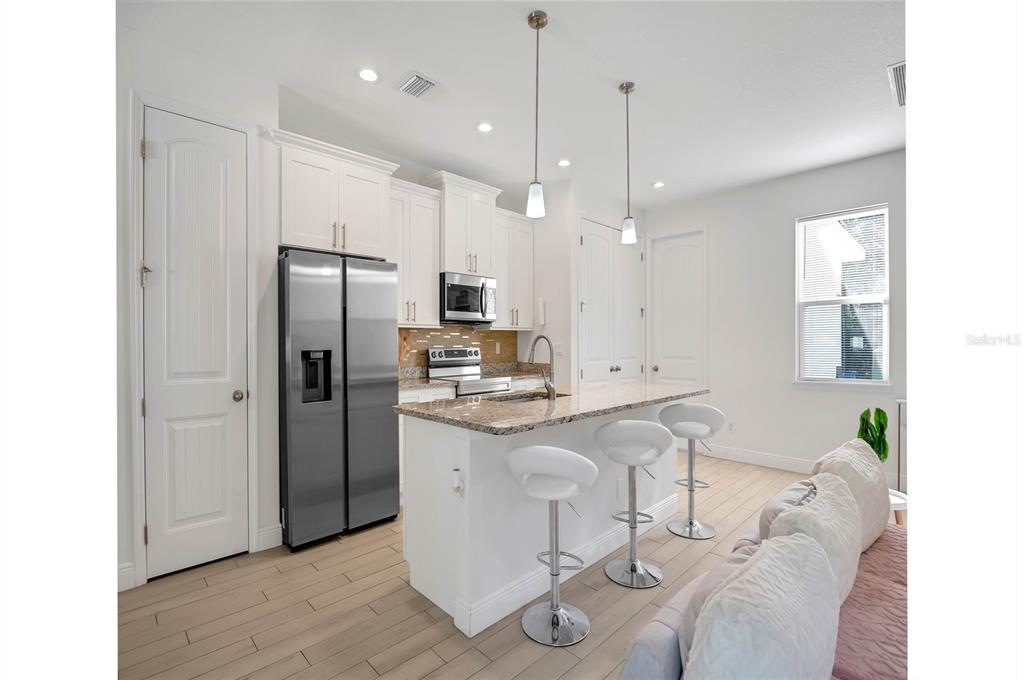 A modern kitchen features white cabinetry, stainless steel appliances, a granite island, and bar stools — 643 FLYNN STREET SE, PALM BAY, FL