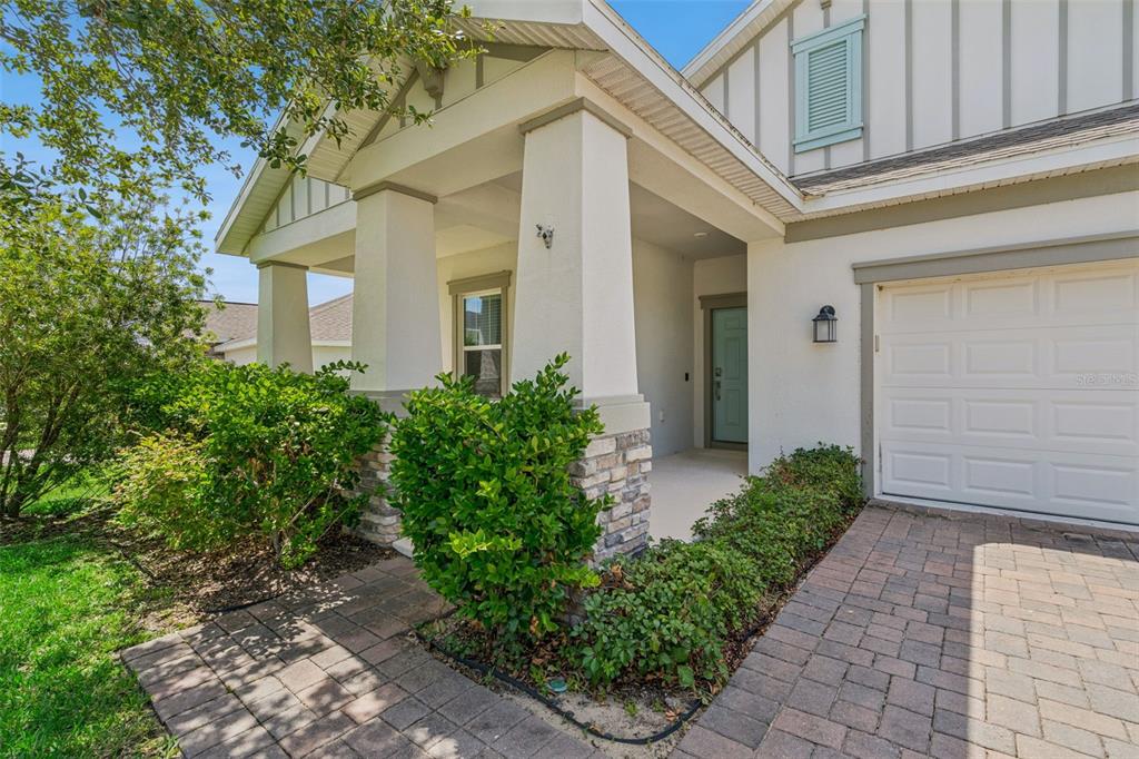 A paved walkway leads to the covered front porch of a house with stone pillars — 897 CARMILLION COURT, GROVELAND, FL