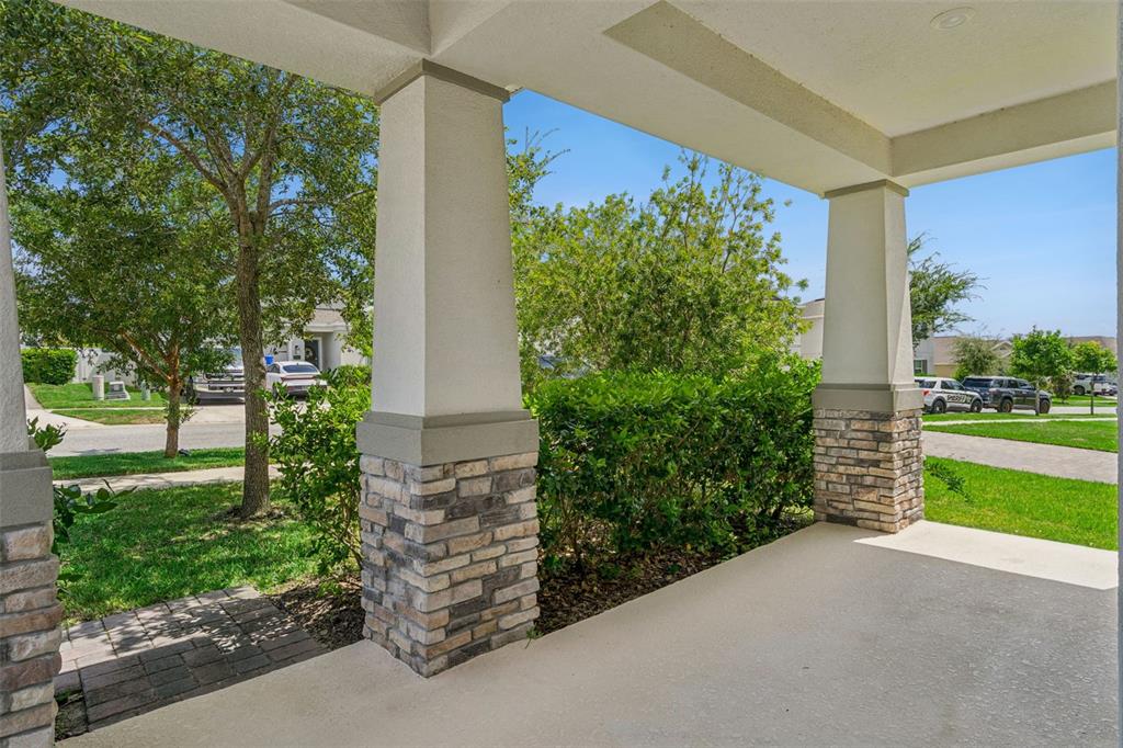 A covered front porch features concrete flooring and two stone-based columns overlooking a residential street — 897 CARMILLION COURT, GROVELAND, FL