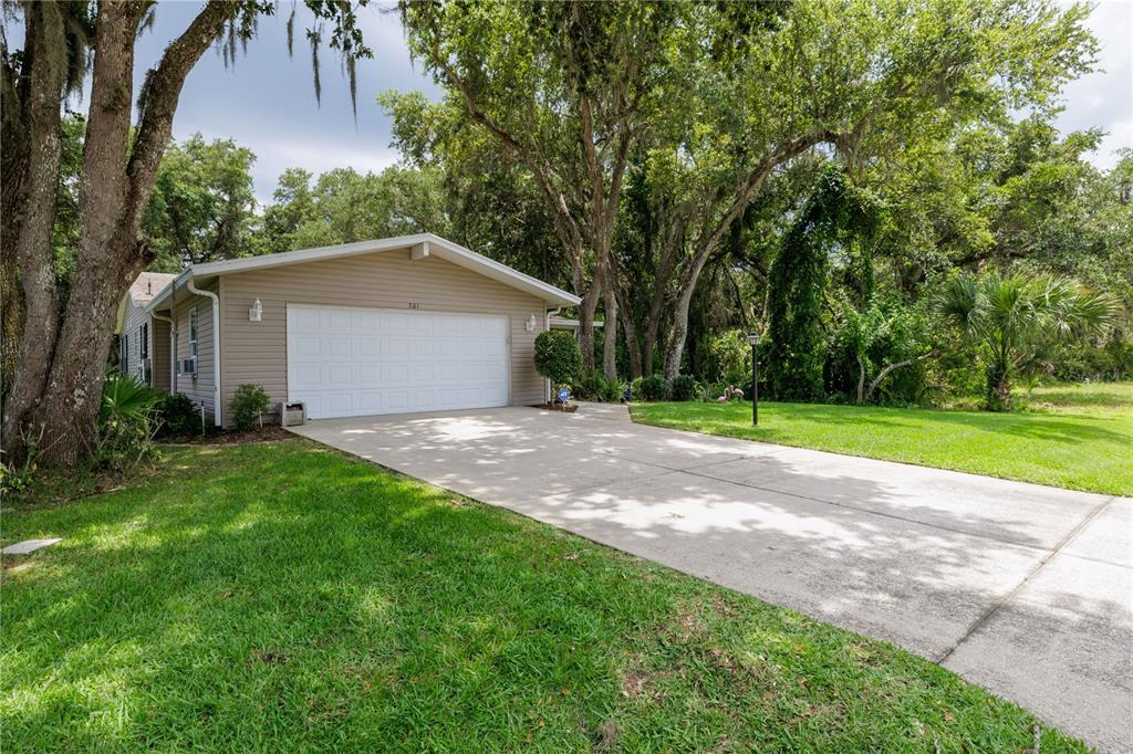 A beige house with a two-car garage and a concrete driveway sits among mature trees — 301 WATERLANDING DRIVE, OAK HILL, FL