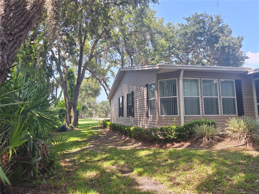 A tan mobile home exterior with a row of windows and surrounding trees and landscaping — 301 WATERLANDING DRIVE, OAK HILL, FL