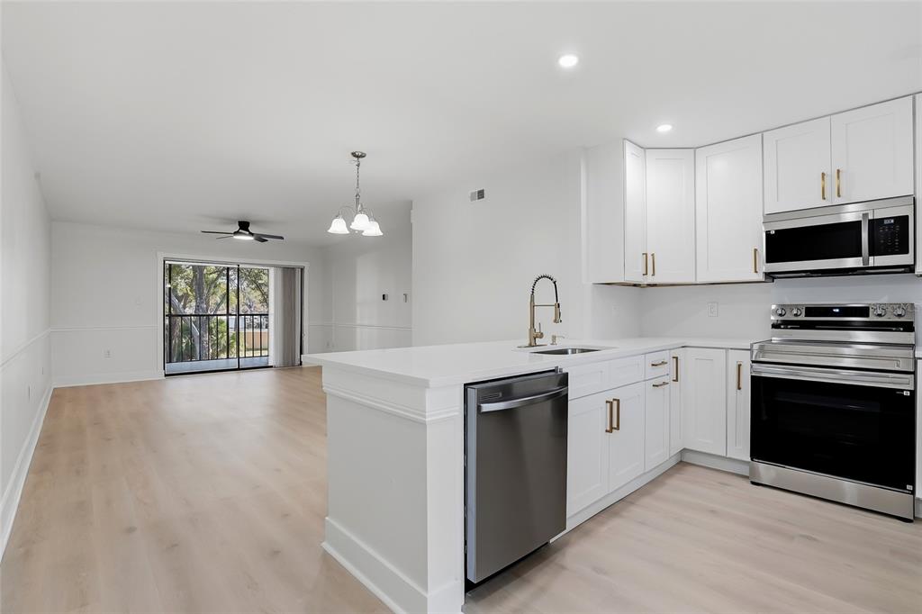 A modern kitchen with white cabinets and stainless steel appliances overlooks an open living area — 2682 SABAL SPRINGS CIRCLE UNIT 204, CLEARWATER, FL