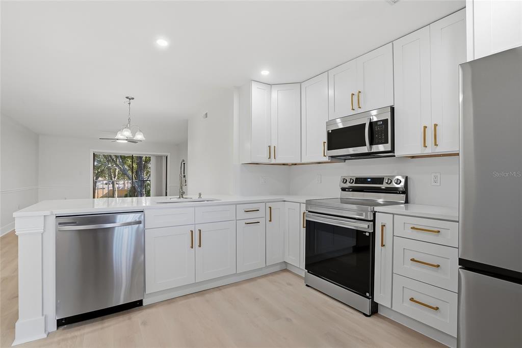 A modern kitchen features white cabinets, stainless steel appliances, and light wood-look flooring — 2682 SABAL SPRINGS CIRCLE UNIT 204, CLEARWATER, FL