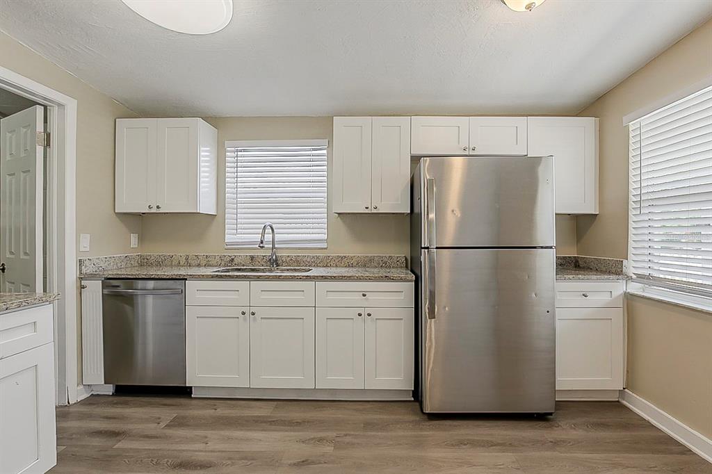 A kitchen features white cabinets, granite countertops, stainless steel appliances, and wood-look flooring — 4010 EMERSON AVENUE S, ST PETERSBURG, FL