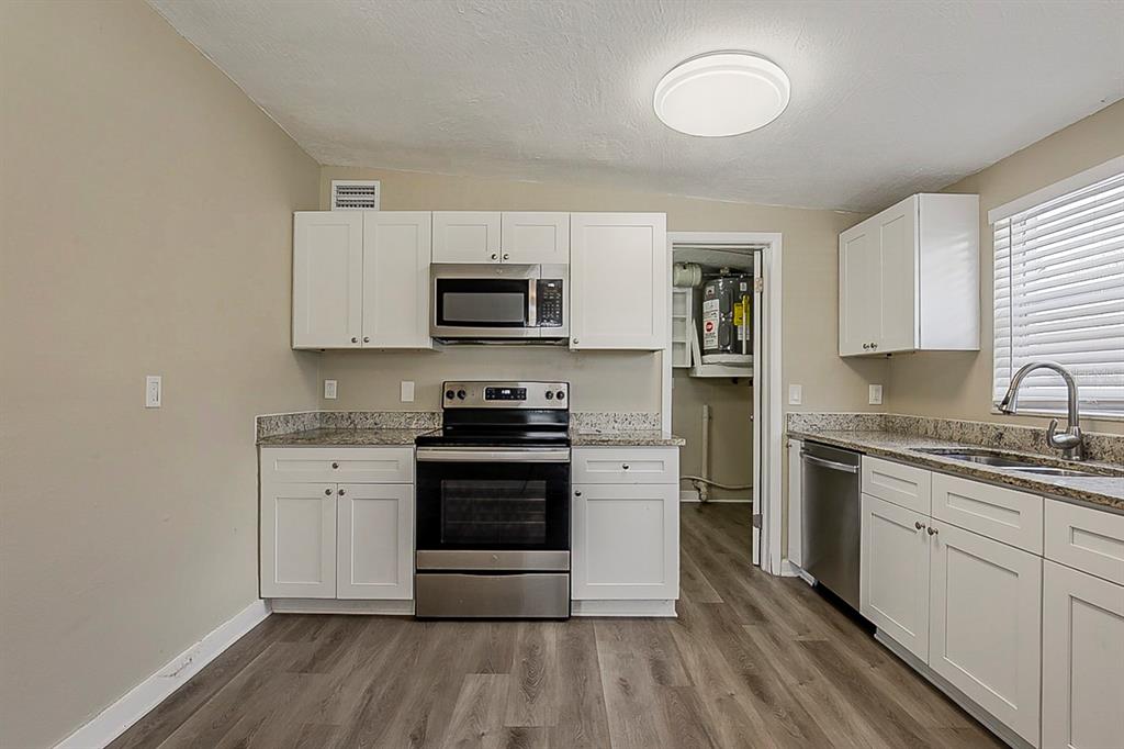 A kitchen features white cabinets, stainless steel appliances, granite countertops, and wood-look flooring — 4010 EMERSON AVENUE S, ST PETERSBURG, FL