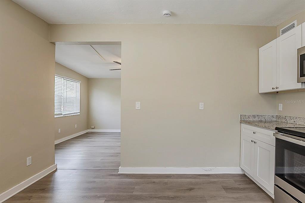 A kitchen area with white cabinets and granite countertops opens into a living room space — 4010 EMERSON AVENUE S, ST PETERSBURG, FL