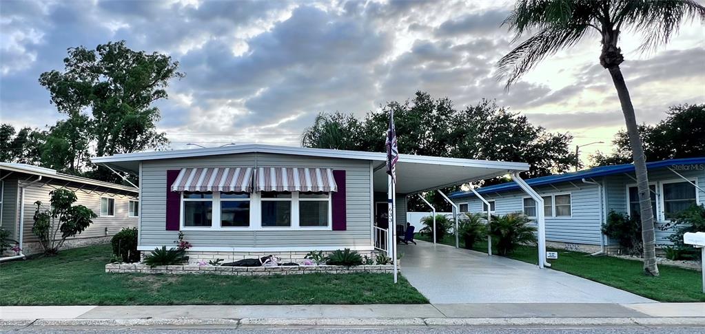 A single-story manufactured home features a carport, striped window awnings, and a palm tree — 1100 BELCHER ROAD S UNIT 633, LARGO, FL