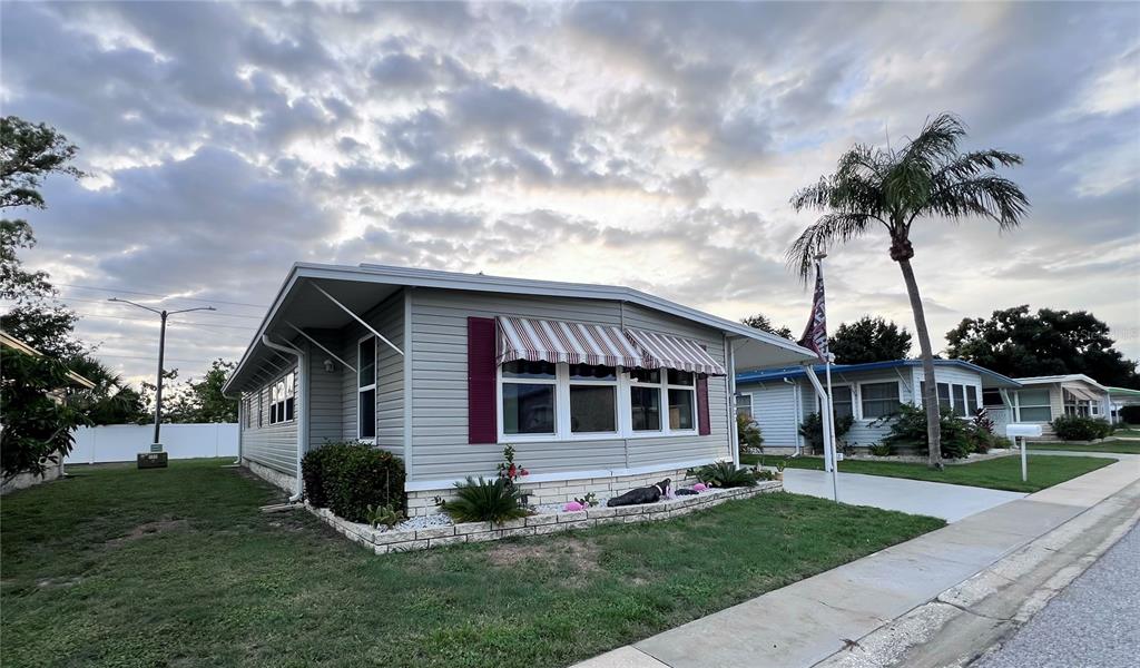 A single-story manufactured home with light gray siding, a striped awning, and a palm tree — 1100 BELCHER ROAD S UNIT 633, LARGO, FL