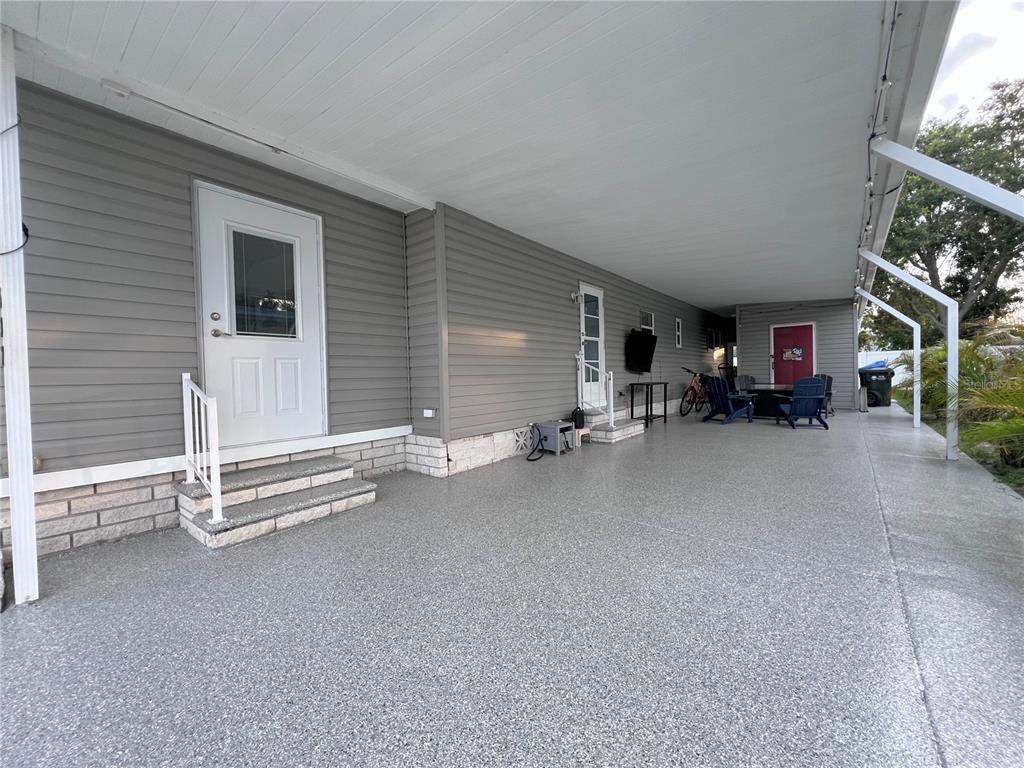 A wide, covered concrete patio features gray siding, two exterior doors, and outdoor furniture — 1100 BELCHER ROAD S UNIT 633, LARGO, FL