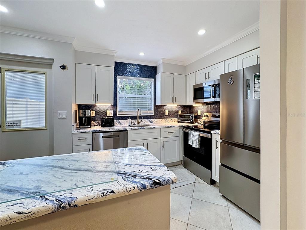 A kitchen features white cabinets, blue mosaic tile backsplash, and blue-veined marble countertops — 120 52ND STREET, HOLMES BEACH, FL