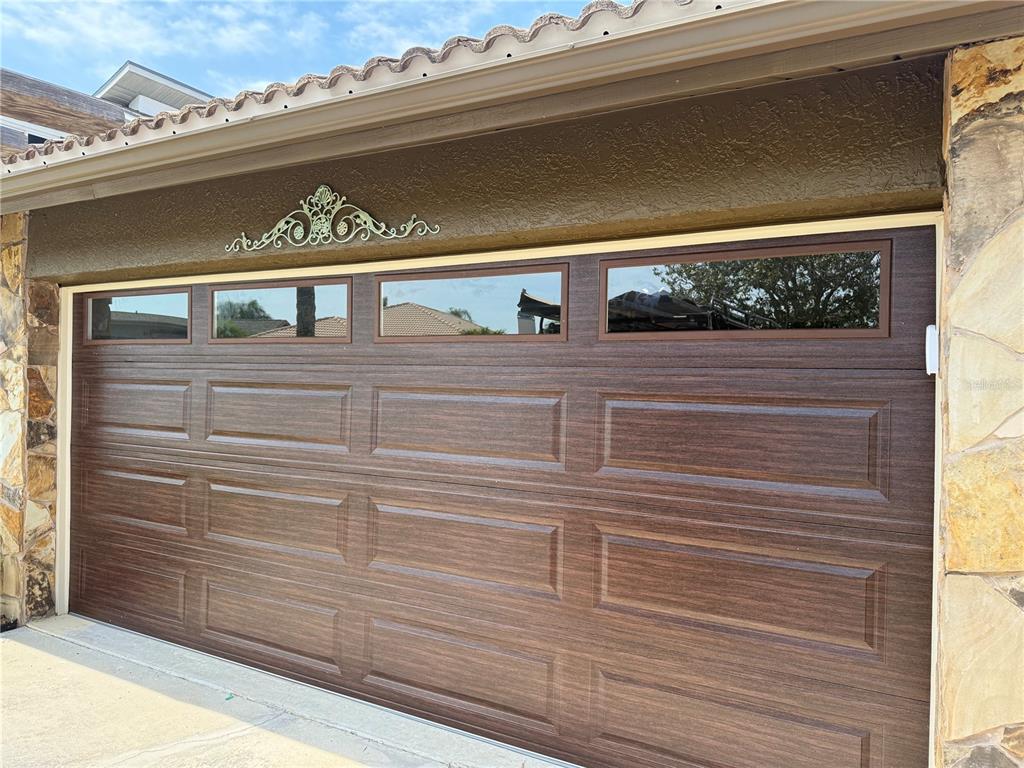 A brown wood-grain garage door with a row of windows and decorative metal scrollwork above — 4554 RICKOVER COURT, NEW PORT RICHEY, FL