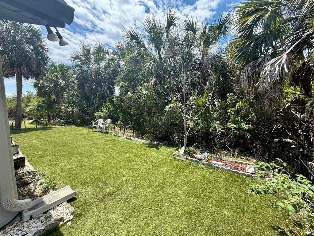 A backyard features artificial turf, a small garden bed, and dense palm trees — 4554 RICKOVER COURT, NEW PORT RICHEY, FL