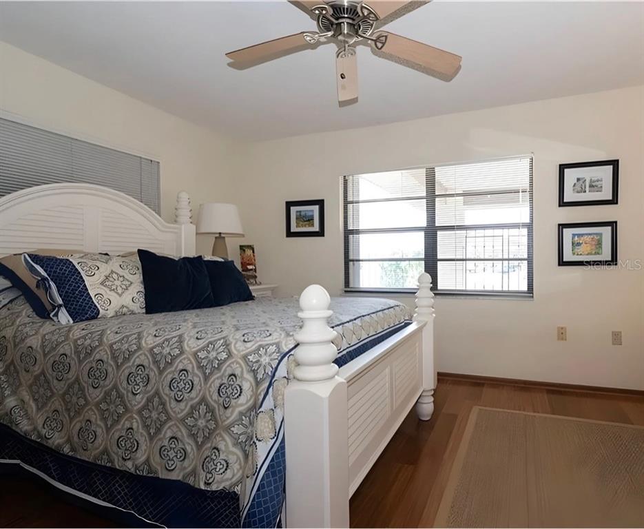 A bedroom features a white bed frame, patterned bedding, a ceiling fan, and wood flooring — 4554 RICKOVER COURT, NEW PORT RICHEY, FL