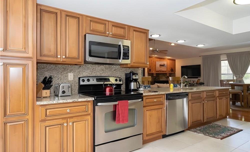 A kitchen with wood cabinets, stainless steel appliances, and granite countertops opens to a living area — 4554 RICKOVER COURT, NEW PORT RICHEY, FL
