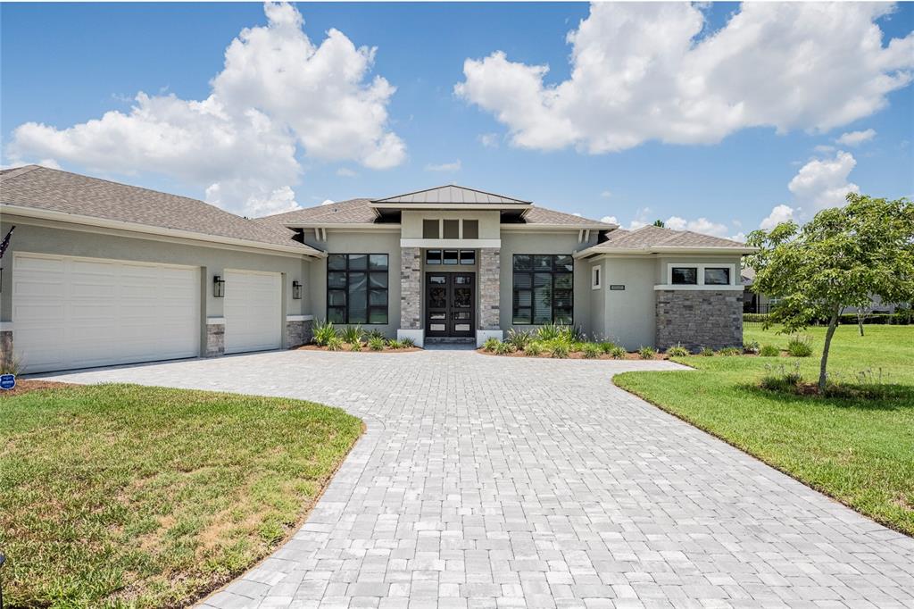 A single-story house with a stone-accented facade, a paved driveway, and a three-car garage — 6545 EMERALD WOODS LANE, LAKELAND, FL